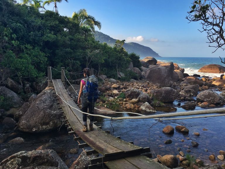 A imagem contém: Mulher atravessando uma ponte que liga a Praia do Sono a Ponta Negra